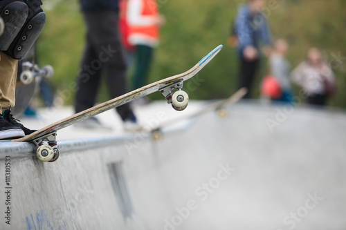 Skater rides on skate board.Skateboarder standing on a ramp in skate park ready to ride skate board and do tricks. Concrete outdoor park, focus on skateboard, feet and shoes