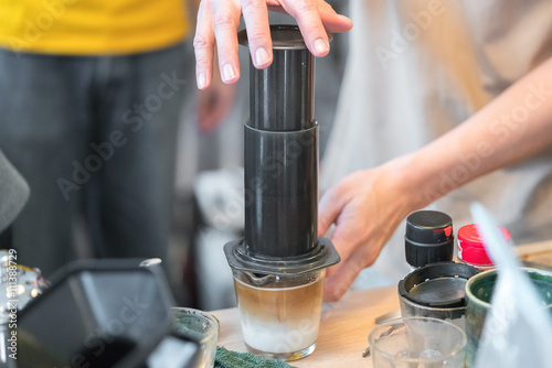 Step by step aero press coffee preparation Bearded barista in blue jeans shirt press aeropress to fill glass with beverage Professional coffee brewing cafe shop
