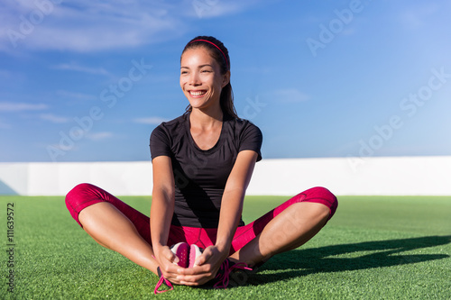 Happy fitness Asian woman butterfly stretching legs in outdoor summer park. Athlete girl doing stretch floor exercises for glutes and inner thigh, groin and hips after running cardio workout.