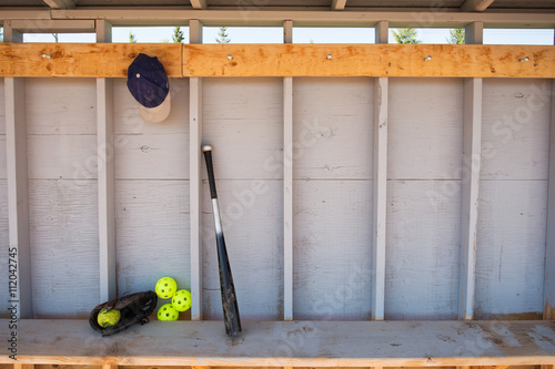 Baseball bat, hat, glove and ball leaning against a wall in a baseball dugout