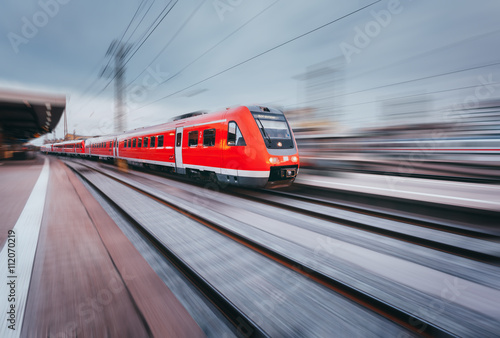 Railway station with modern high speed red passenger train at sunset in Nuremberg, Germany. Railroad with motion blur effect vintage toning. Industrial landscape