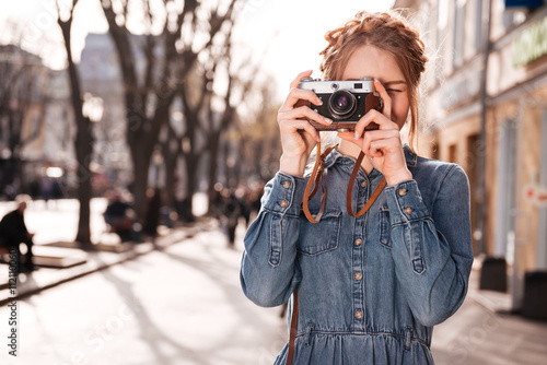 Concentrated woman taking pictures outdoors using old vintage camera