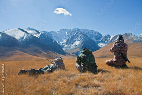 Three hunters looking through binoculars in mountains of Tien Sh