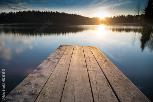 sunset on the lake. Old wooden pier into the horizon and sun lights. Beginning on a new day