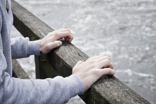 Depressed Young Man Contemplating Suicide On Bridge Over River