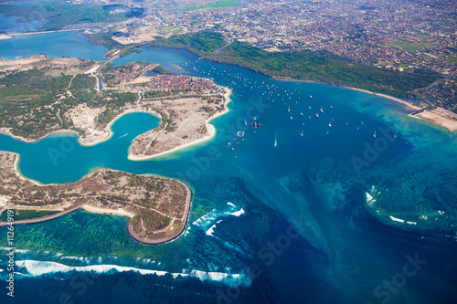 Aerial photo of Pulau Serangan ( turtle island ) with sand beach, surfing spots, sailing yacht and fisher boats at anchor in sea bay harbour and part of Denpasar and Sanur on Bali island, Indonesia