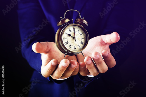 Businessman holding old clock in hands on dark background