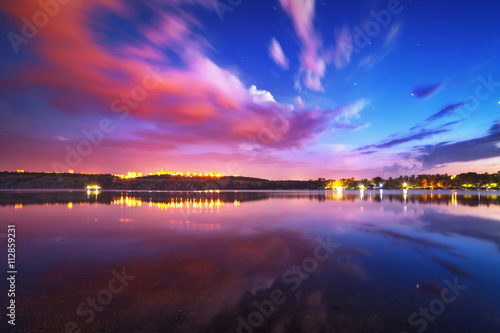 Colorful night landscape on the lake with blue sky and moving clouds reflected in water. Nature background