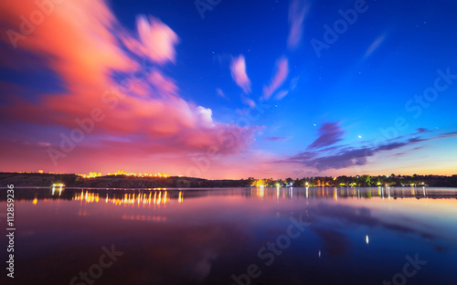 Colorful night landscape on the lake with blue sky and moving clouds reflected in water. Nature background