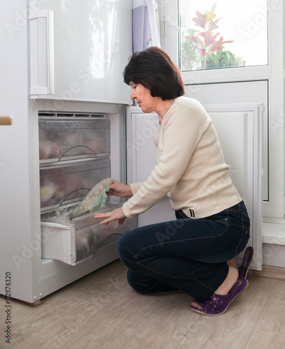 woman near open freezer of refrigerator.