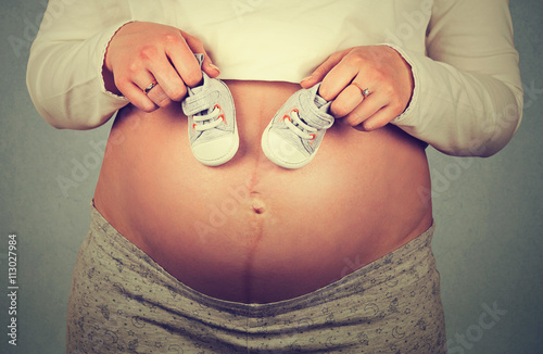 Small shoes for the unborn baby on the belly of pregnant woman