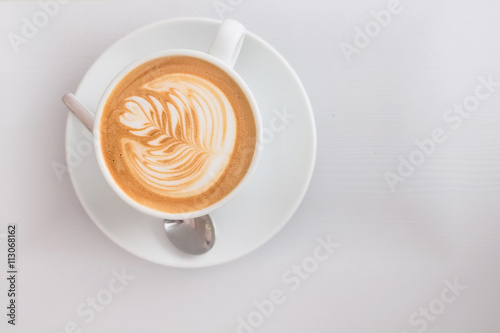 Cup of flat white coffee with milk foam pattern on a white wooden surface. Top view.
