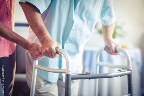 Senior woman helping senior man to walk with walker