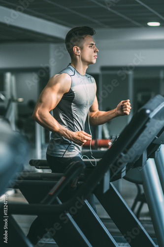 Young man in sportswear running on treadmill at gym