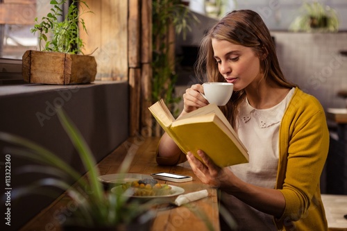 Casual woman reading a book while drinking