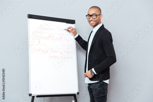 Smiling african man in glasses writing business plan on flipchart