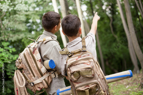 two boys go hiking with backpacks on a forest road bright sunny