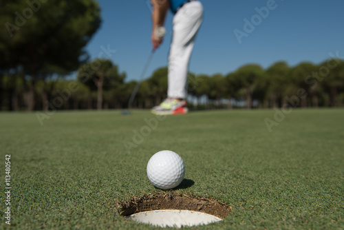 golf player hitting shot, ball on edge of hole