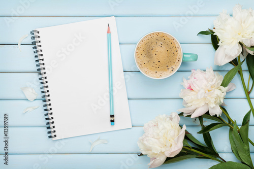 Morning coffee mug, empty notebook, pencil and white peony flowers on blue wooden table, cozy summer breakfast, top view, flat lay