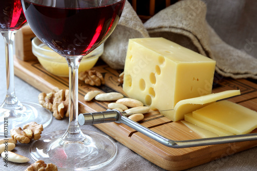 Piece of cheese on a board, wine glasses and nuts..