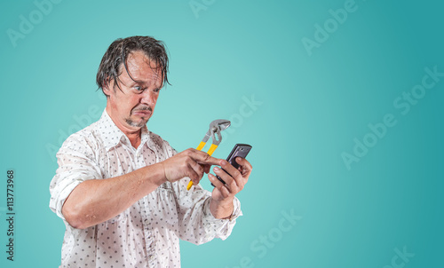 nasser Mann mit Wasserpumpenzange sucht auf Smartphone nach Hilfe