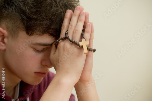 Teenage boy praying with a rosary
