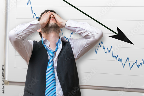 Bad investment or economic crisis concept. Businessman is disappointed from losing in stock exchange. Chart with arrow down on whiteboard in background.