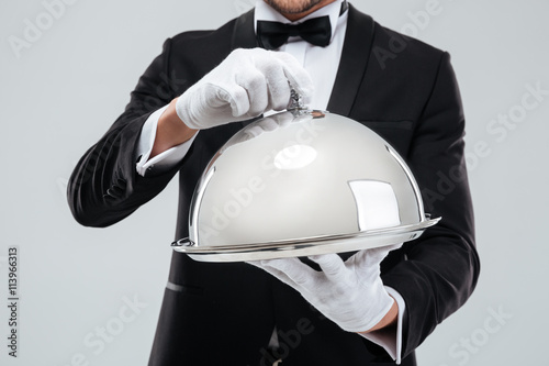 Serving tray with cloche holded by butlers hands in gloves