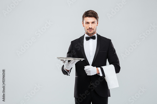 Attractive butler in tuxedo standing and holding silver empty tray