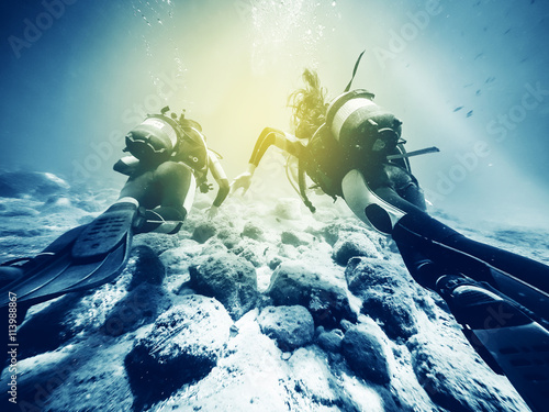 Two divers swimming close to the ocean floor.