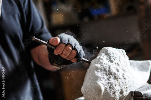 Close up of senior sculptor hands working on his marble sculpture in his workshop with hammer and chisel