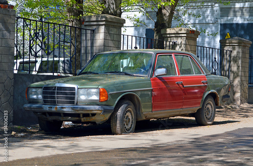 Брошенная старый автомобиль зеленого цвета без номеров, стоящbq около ограды во дворе дома днем