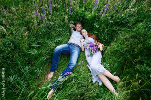 man and woman embracing lying in grass on a meadow with bouquet of lupines