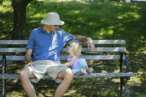Caring father sits with the kid on a wooden bench