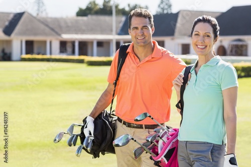 Portrait of couple carrying golf bags 