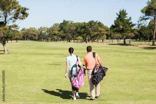 Rear view of couple carrying golf bags