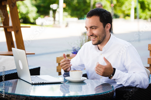 Work and relax. Online conference. Businessman dressed in shirt working with laptop, talking by skype at the park cafe outdoors