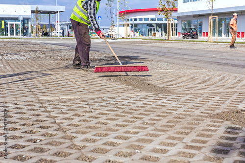 Worker is cleaning new parking place with red broom