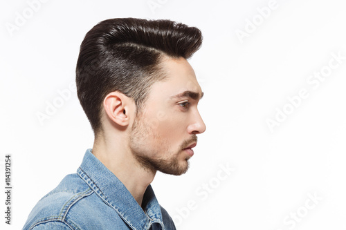 Closeup profile of model man injeans shirt demonstrating his modern hairstyle over white background in studio. Hairdressing concept.
