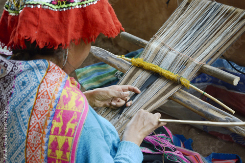 Peruvian woman in traditional clothing weaving cloth on a hand loom