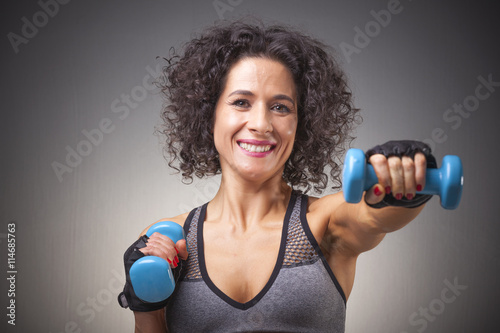 Fit woman training with dumbbells on grey bakground