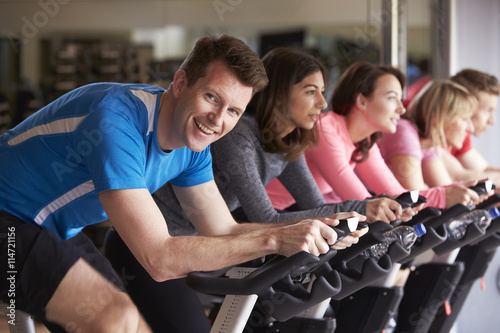Man in a spinning class at a gym turning to smile at camera