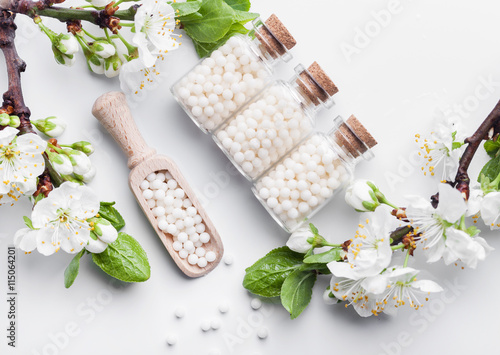 homeopathic pills with spring flowers on white wooden background