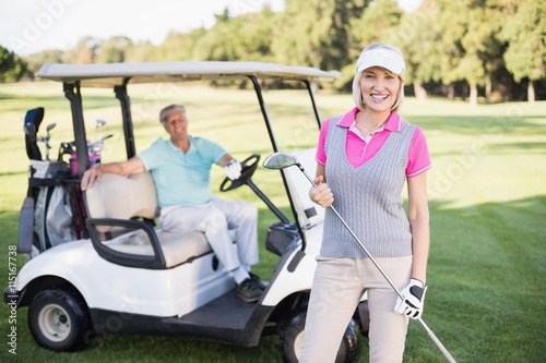 Smiling mature woman standing by man in golf buggy