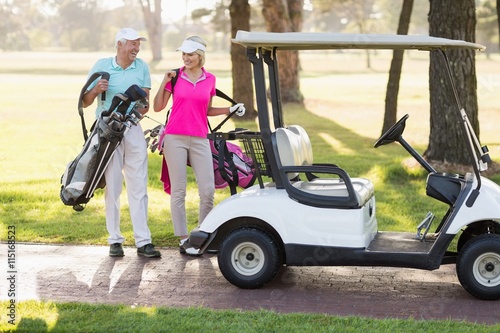 Happy mature golfer couple by golf buggy