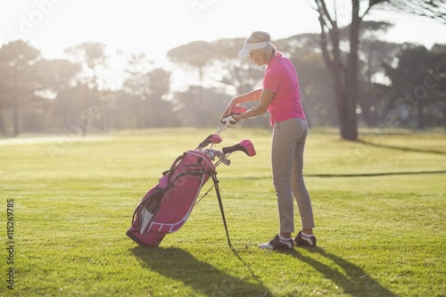 Side view of woman putting golf club in bag 