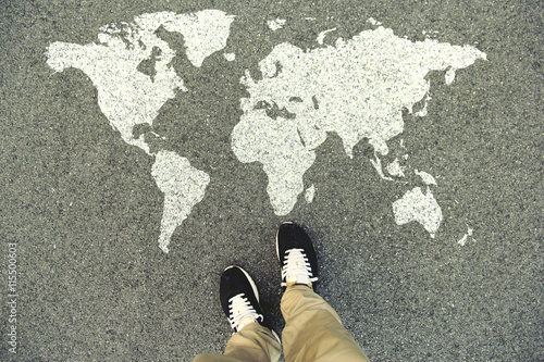 World map on an asphalt road. Top view of the legs and shoes. POV