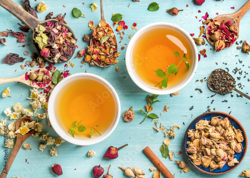Dwie szklanki zdrowej herbaty ziołowej z miętą, cynamonem, suszoną różą i rumiankiem w łyżkach na niebieskim tle