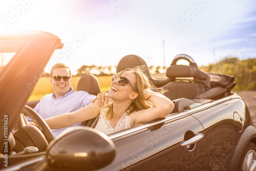 Mit dem Cabrio unterwegs - Verliebtes Paar im Cabrio lacht und ist glücklich 