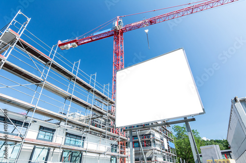 Leeres Schild auf Baustelle für modernen Neubau mit Gerüst und Kran im Hintergrund